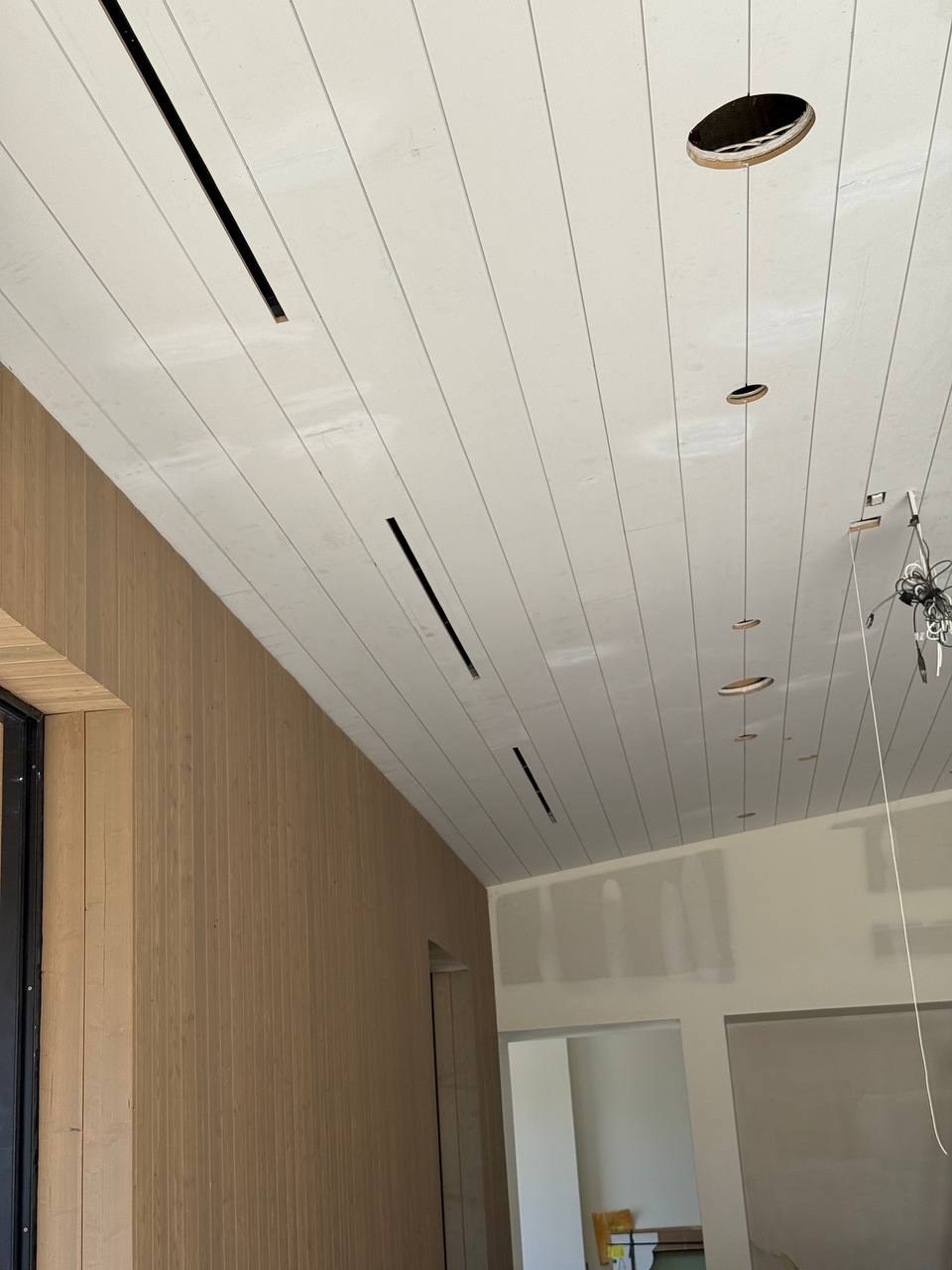 Multiple slim linear slot grilles in a white plank ceiling during finish construction